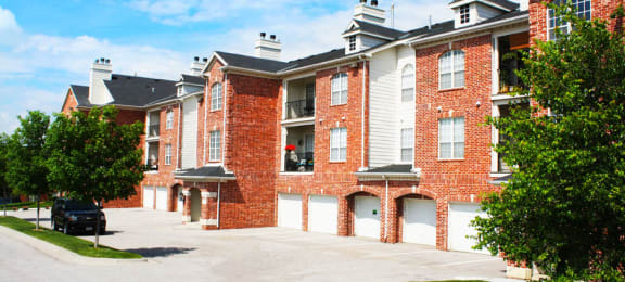 Luxury apartments with red brick exterior, attached garages, lush landscaping, and scenic views at Lenox Village Apartments in Lincoln, Nebraska