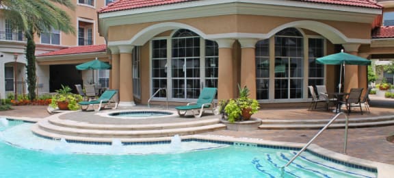 Luxury apartments with resort-style pool with fountains, pool-side lounge chairs, spa, and palm trees at Tuscany Court Apartments in Houston.