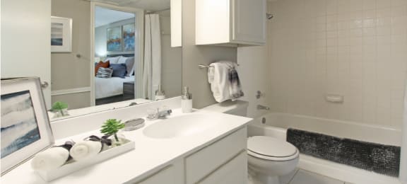 Spacious bathroom with white cabinets and white porcelain tile at Preston Village Apartments in North Dallas
