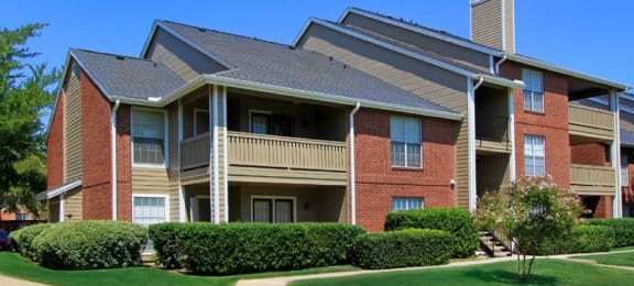 Luxury apartments with red brick exteriors, beautiful landscaping, and spacious balconies at Preston Village Apartments in North Dallas