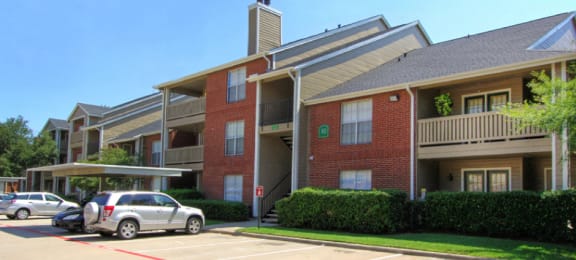 Luxury apartments with red brick exteriors, beautiful landscaping, and spacious balconies at Preston Village Apartments in North Dallas
