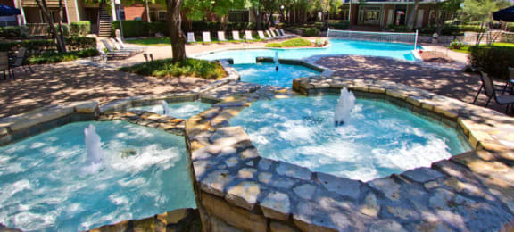 Luxury apartments with beautiful fountains, beautiful landscaping, swimming pool with poolside lounge chairs, and scenic views at Preston Village Apartments in north Dallas