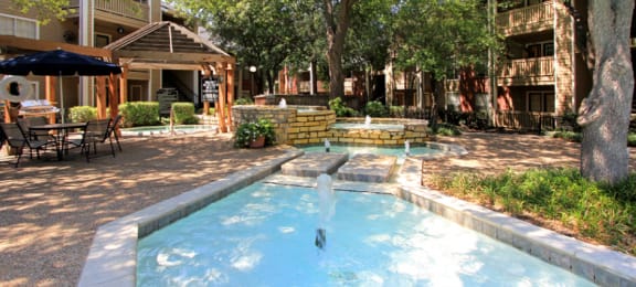 Luxury apartments with beautiful fountains, beautiful landscaping, gazebo, spa and swimming pool with poolside lounge chairs, grilling station and scenic views at Preston Village Apartments in north Dallas