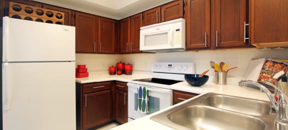 Spacious kitchen with honey brown toned cabinets, lots of counter space, white appliances, tile floor and recessed ceiling at Tuscany Oaks Apartments in Houston
