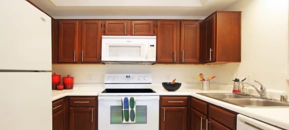 Spacious kitchen with honey brown toned cabinets, lots of counter space, white appliances, tile floor and recessed ceiling at Tuscany Oaks Apartments in Houston