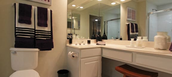 Spacious bathroom with oval soaking tub with glass enclosure, cultured marble vanity, glass shower, and built-in vanity at Tuscany Oaks Apartments in Houston.