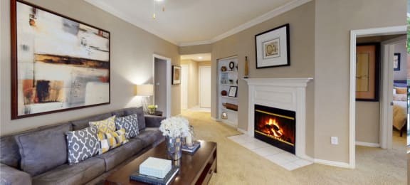 Spacious living room with wood-burning fireplace with glass doors, ceiling fan, crown molding, and built-in bookshelves at Tuscany Apartments in Houston.