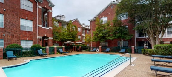Luxury apartments with red brick exteriors, large swimming pool with spacious sundeck, grill, beautiful landscaping, lush landscaping, chaste trees, and pool-side lounge seating at Tuscany Apartments in Houston.