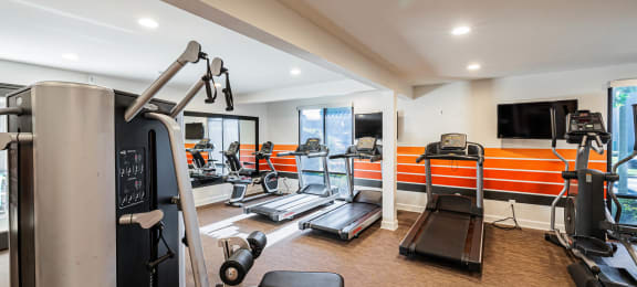 a gym with cardio equipment and a television on the wall