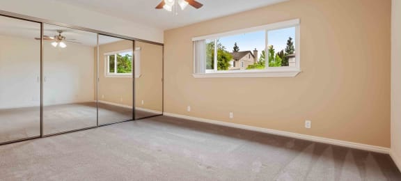 Apartments for Rent in Fremont - Logan Park - Large Empty Bedroom with Mirrored Closet, Ceiling Fan, Carpet, and Window