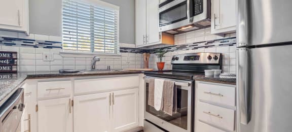 San Jose CA Apartments for Rent - Los Gatos Creek - Kitchen with Stainless-Steel Appliances, White and Blue Backsplash, a Window, and White Cabinetry