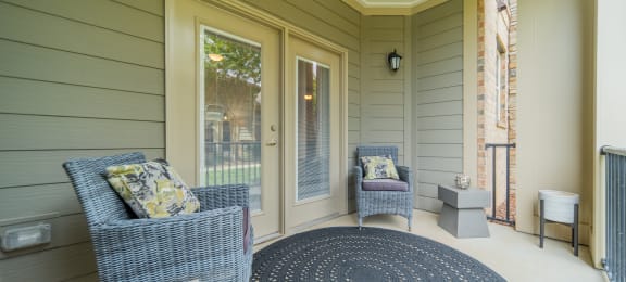 a covered porch with two chairs and a rug