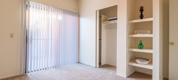 Bedroom with closet next to shelves and sliding glass door with blinds
