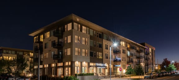a nighttime view of a large apartment building with a parking lot in front of it