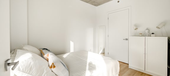 a bedroom with white bedding and white walls and a wooden floor