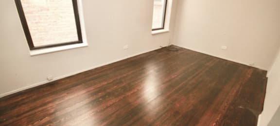 an empty room with hardwood floors and two windows