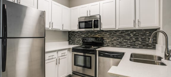 Townhomes in Houston, TX - The Maroneal - Modern Kitchen with White Countertops, Stainless Steel Appliances, Hardwood Flooring, and White Cabinetry