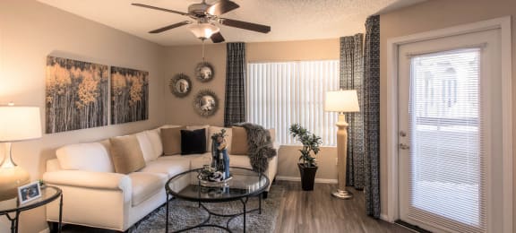 Apartments in Ahwatukee, Foothills, AZ - Pacific Bay Club - Living Room with Wood-Style Plank Flooring, Stylish Decor, Ceiling Fan, Large Window, and Door to the Private Patio