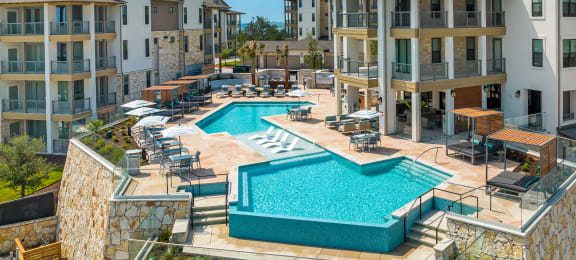 an aerial view of a resort style pool with lounge chairs and a stone wall