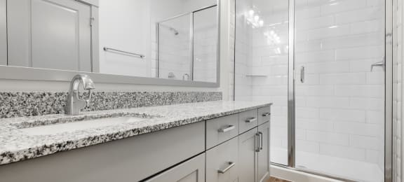 a bathroom with white cabinets and granite counter tops and a shower