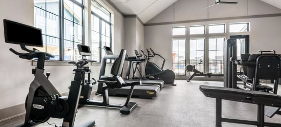 a gym with cardio equipment and weights in a building with large windows
