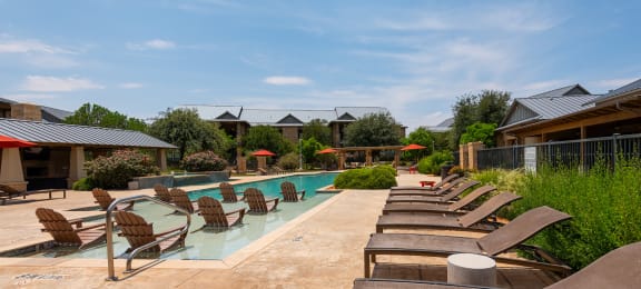 a pool with lounge chairs and umbrellas at the whispering winds apartments in pearland,