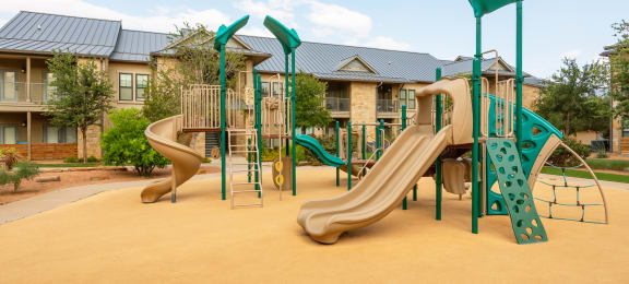 a playground with two slides and a climbing structure in front of an apartment building