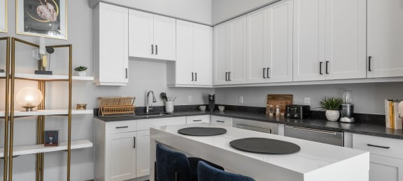 a kitchen with white cabinets and a white island with black chairs