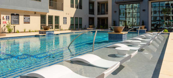 a large swimming pool with white lounge chairs in front of a building
