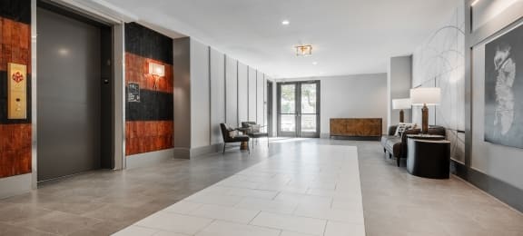 the lobby of a condo with a large white tiled floor and a glass door
