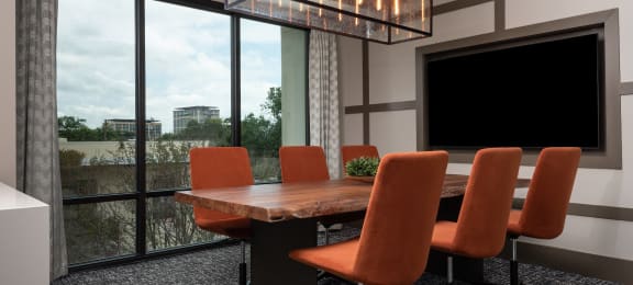 a conference room with a large screen tv and a wooden table with orange chairs