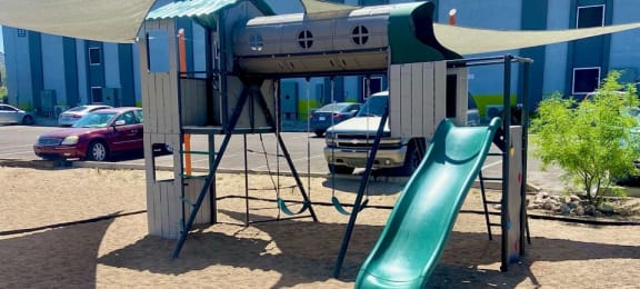 a swing set with a slide in a parking lot with a building in the background