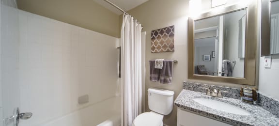 Bathroom with tub/shower combo, white cabinets, modern grey and white counters.
