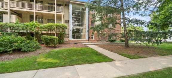 a sidewalk in front of an apartment building with grass and trees