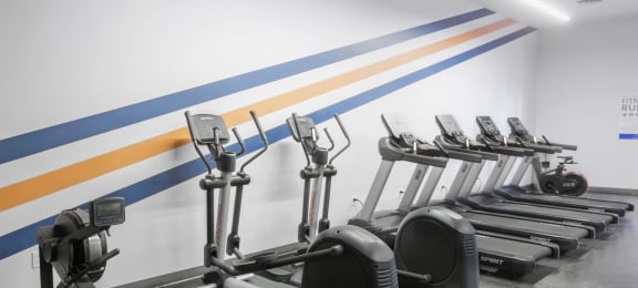 a row of exercise machines in front of a white wall with blue and yellow stripes