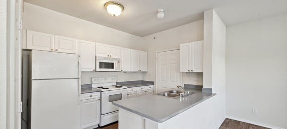 Apartments in North Dallas TX - Tivoli - Galley Kitchen with White Cabinetry, Grey Countertops, and All White Appliances