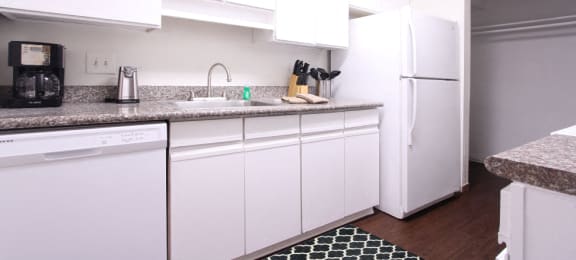 Bright white kitchen with granite countertops and hardwood floors at at Briarwood Apartments in Houston.