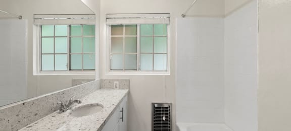 Van Nuys Apartments - Colonial Manor - Grey Countertop, White Bathtub, and Large Mirror