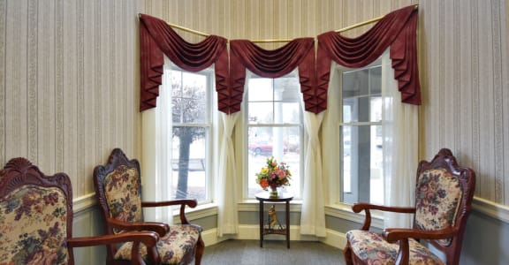a living room with chairs and windows with curtains