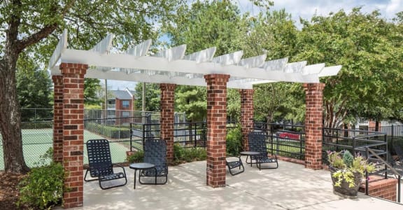 a patio with a pergola and a tennis court in the background