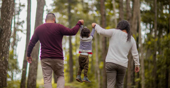 a family walking through the woods holding hands and a child jumping