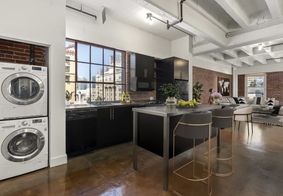 Kitchen with a washing machine and a kitchen island with chairs and a counter top at South Park Lofts, Los Angeles, California