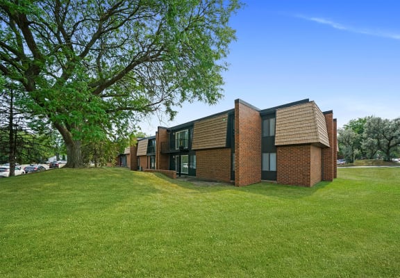 a row of brick apartments on a green lawn with a tree