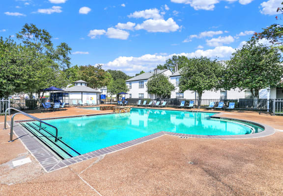 the large swimming pool and sundeck surrounded by lush trees at Rock Creek Apartments