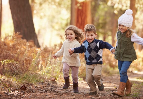 Group of Children in Winter Clothing Running in Forest
