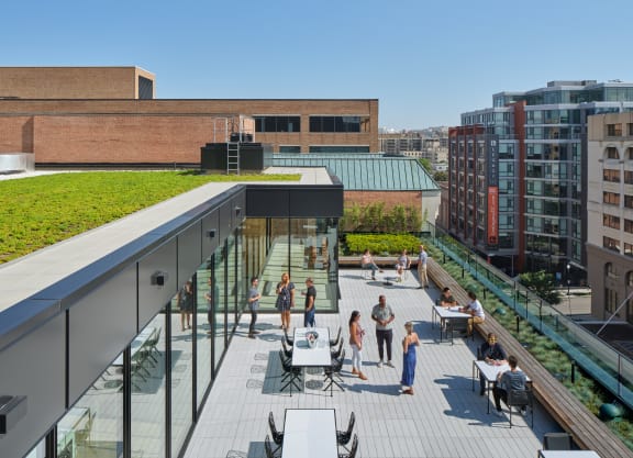 a roof deck with tables and chairs and a green roof on top of a building