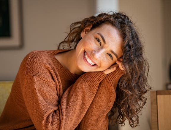 a woman sitting on a couch with her head on her hand and a big smile on her