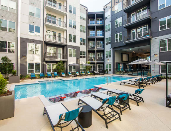 an outdoor pool with lounge chairs and tables at an apartment building