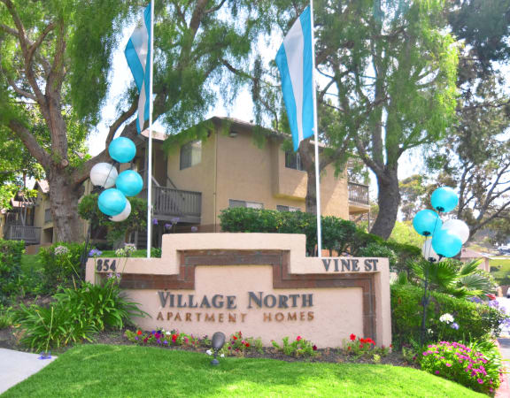 a sign for village north apartment homes with blue and white balloons in front of it