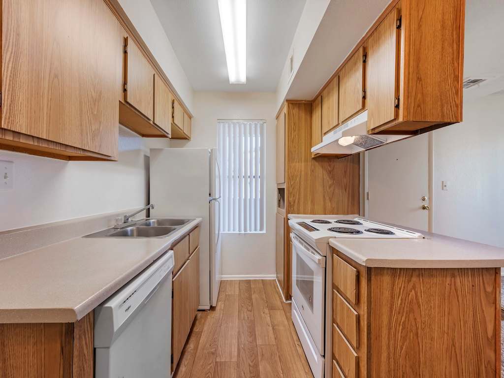 Galley kitchen with wood cabinets and white appliances — view 1 at Glen Oaks Apartments.